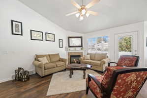 Living room featuring lofted ceiling, dark wood-type flooring, a tile fireplace, and ceiling fan