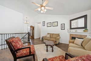 Living room with dark wood-style floors, a chandelier, a fireplace, ceiling fan, and high vaulted ceiling