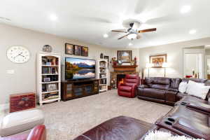 Carpeted living area featuring a stone-faced fireplace with a wood mantel, recessed lighting, and a ceiling fan with light fixture