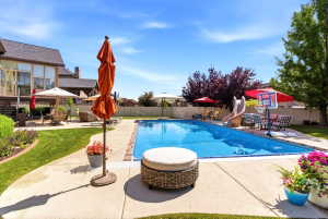 Expansive backyard featuring a rectangular swimming pool with brick coping, a surrounding concrete patio, and mature landscaping