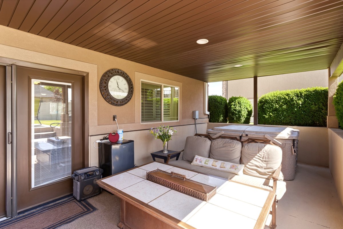 Covered outdoor patio featuring a neutral stucco exterior, a built-in spa, a sliding glass door, a window with horizontal blinds, and a brown paneled ceiling