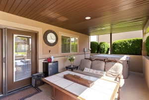 Covered outdoor patio featuring a neutral stucco exterior, a built-in spa, a sliding glass door, a window with horizontal blinds, and a brown paneled ceiling