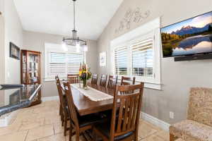 Vaulted ceiling dining area featuring tile flooring, plantation shutters, and a granite-topped bar