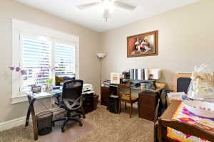 Room featuring a ceiling fan, a window with white louvered shutters, light-colored walls, and textured carpeting