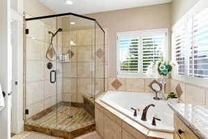 Bathroom featuring a corner soaking tub with bronze fixtures, a glass-enclosed shower with tiled walls and floor, and plantation shutters on the window