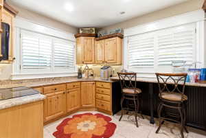 Corner kitchen featuring natural wood cabinetry with dark hardware, speckled countertops, and an integrated cooktop