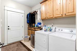 Laundry area featuring upper wood cabinetry, a utility sink, a hanging rod, and light-toned tile flooring