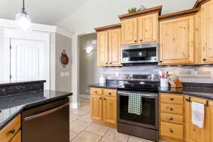 Kitchen featuring light wood cabinetry with dark hardware, black stone countertops, and a tile backsplash