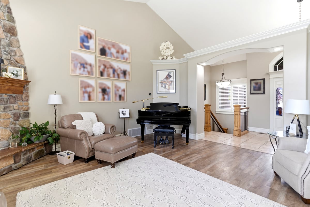 Vaulted ceiling living area featuring a stone fireplace with wood mantle, wood-finish flooring, a grand piano, and an arched entry