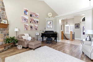 Vaulted ceiling living area featuring a stone fireplace with wood mantle, wood-finish flooring, a grand piano, and an arched entry