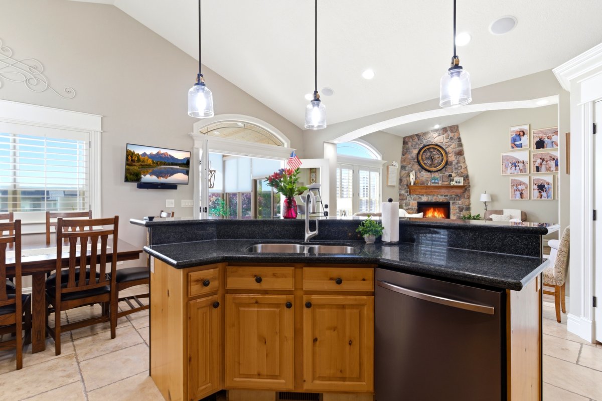Kitchen island featuring a stainless steel sink, dark stone countertop, light wood cabinetry, and a black dishwasher