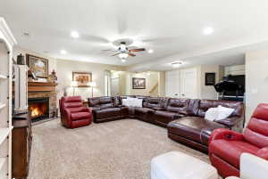 Spacious carpeted living area featuring a stone-faced fireplace with a wood mantle, recessed lighting, and a ceiling fan