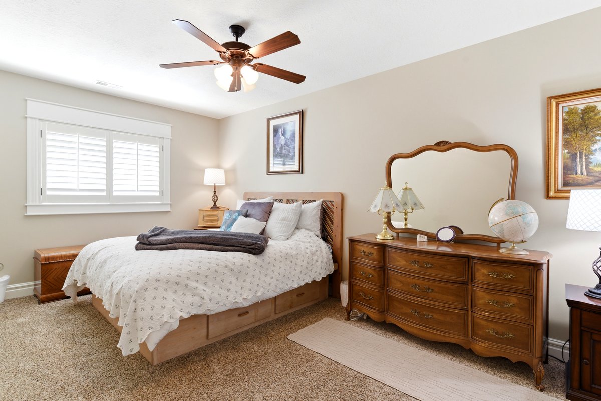 Carpeted room featuring a ceiling fan with light fixture, window with white plantation shutters and trim, and neutral wall paint