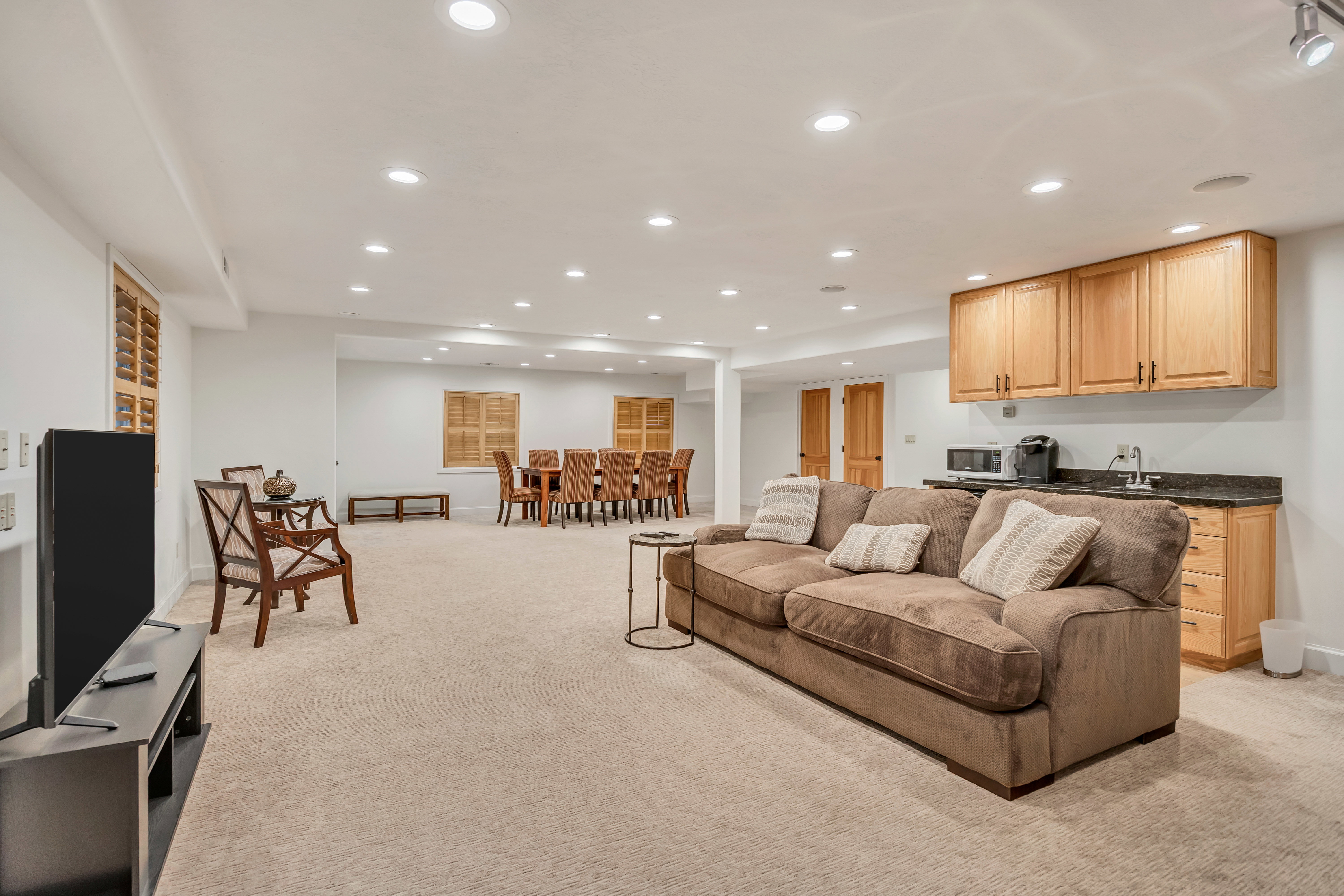 Carpeted recreation area featuring recessed lighting, a wet bar with wood cabinetry and dark countertops, and interior window shutters