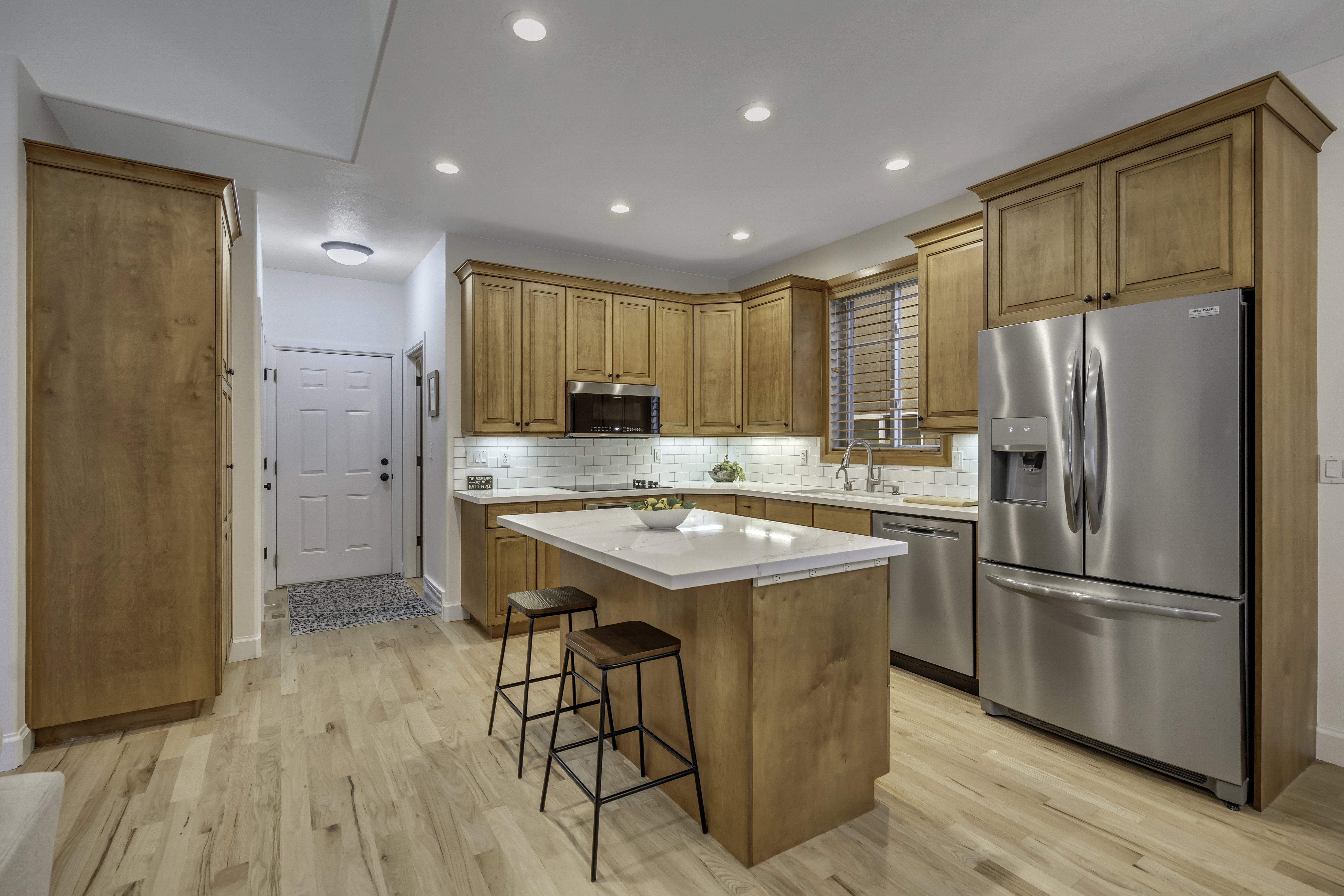 Spacious kitchen featuring light wood cabinetry, a central island with a white countertop, stainless steel appliances, and wood-finish flooring