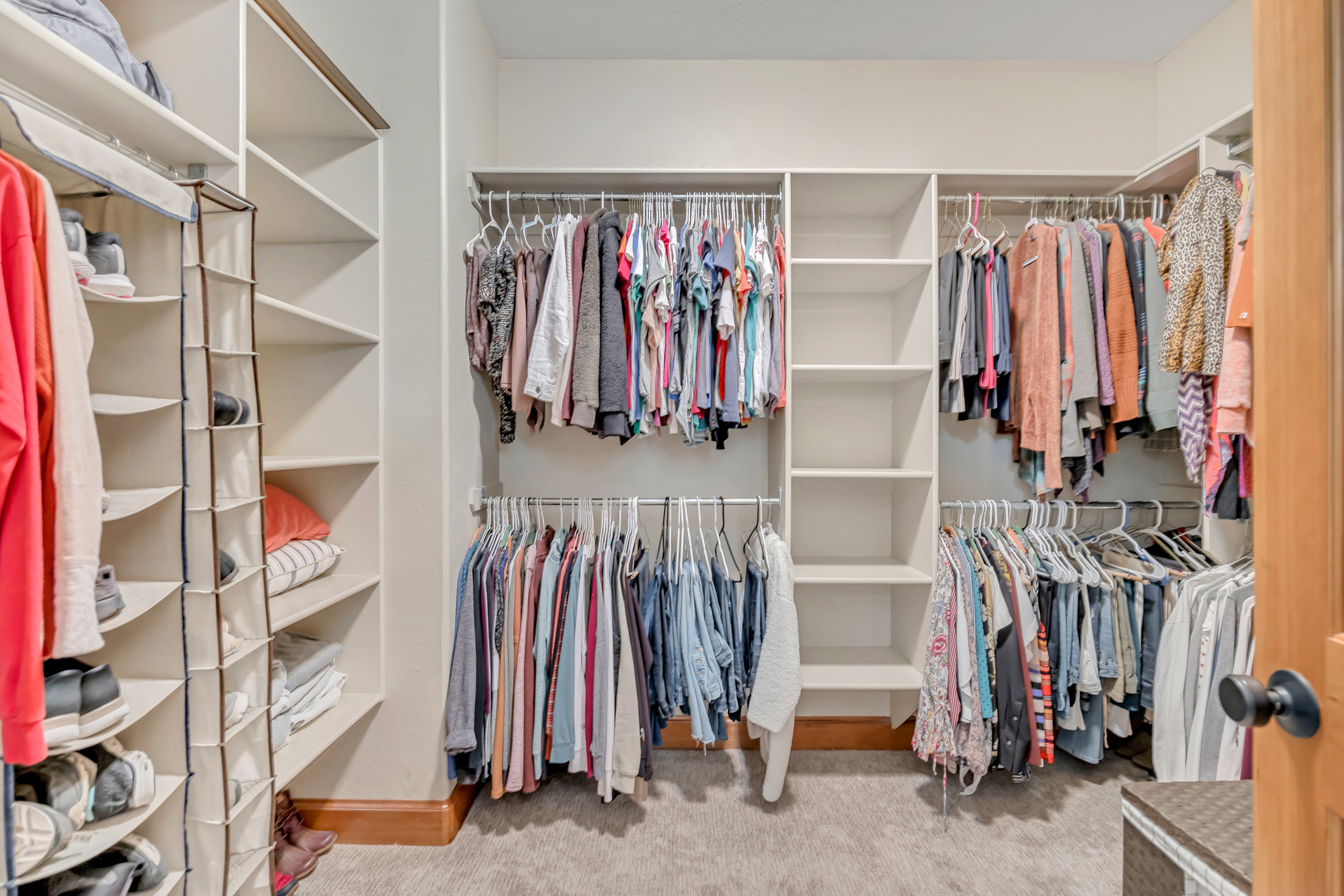 Spacious walk-in closet featuring extensive built-in shelving, multiple hanging rods, and soft carpet flooring