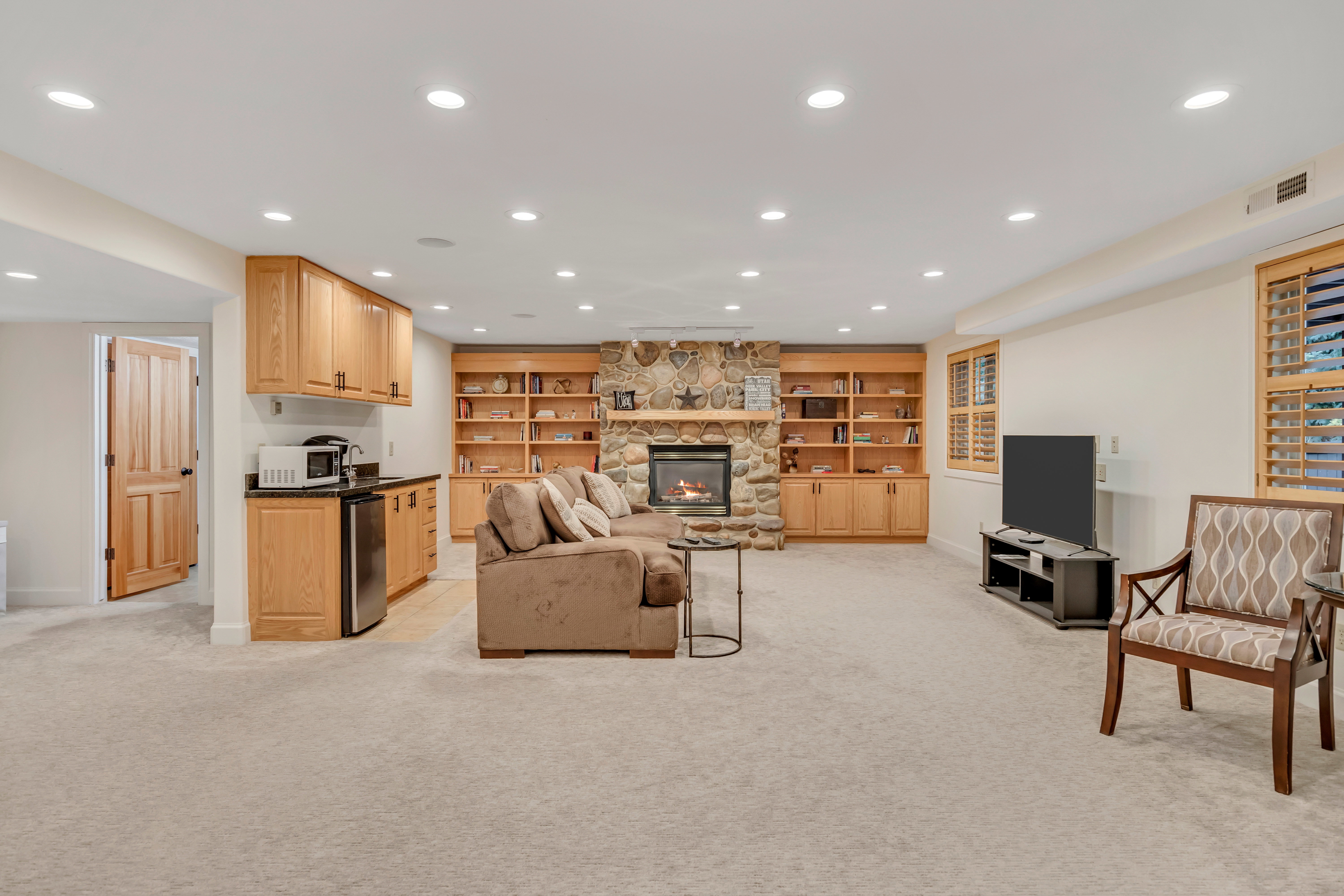 Spacious recreation room featuring recessed lighting, a stone-faced fireplace, and custom built-in cabinetry with shelving