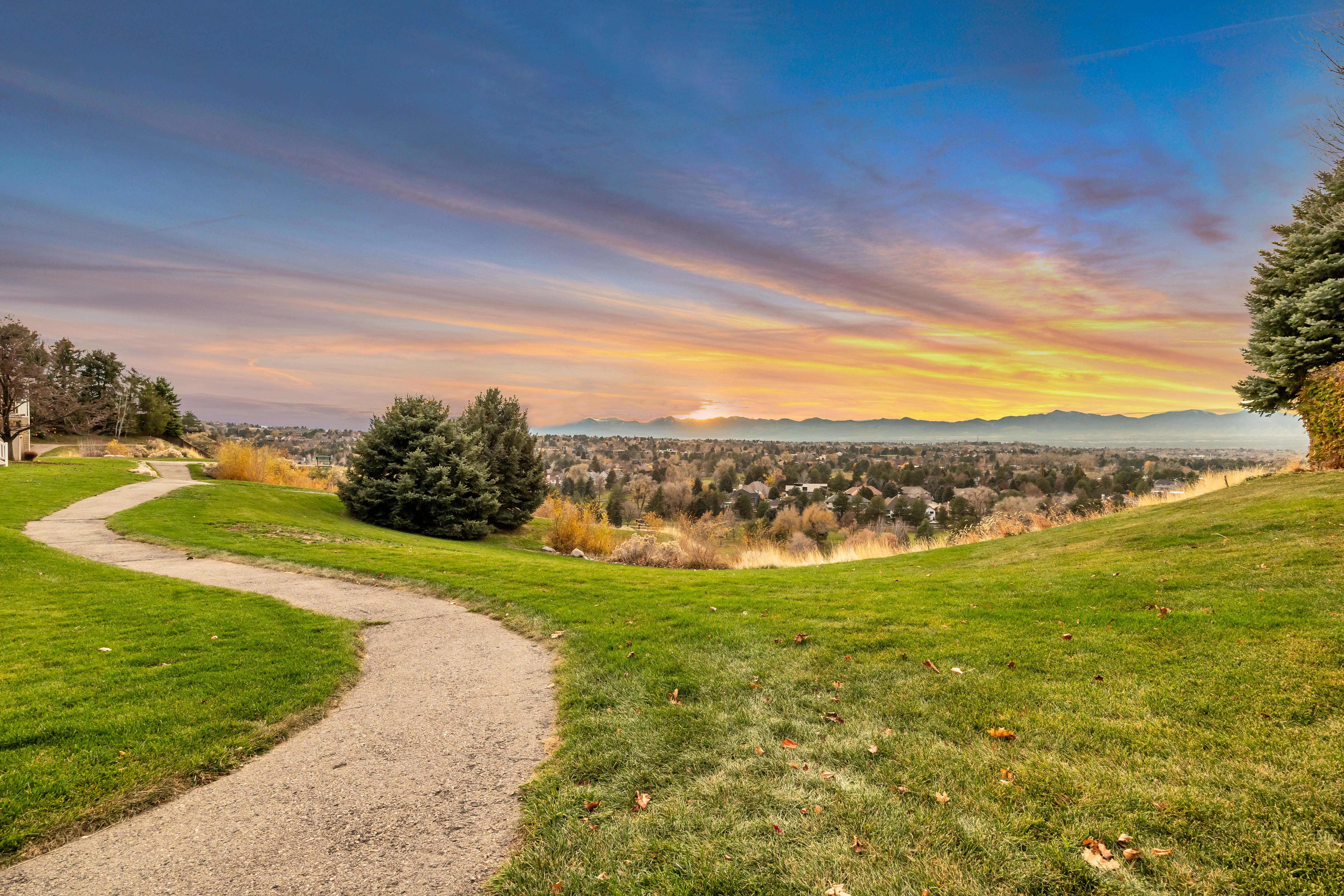 Winding pathway across a green lawn with a distant cityscape and mountain range backdrop