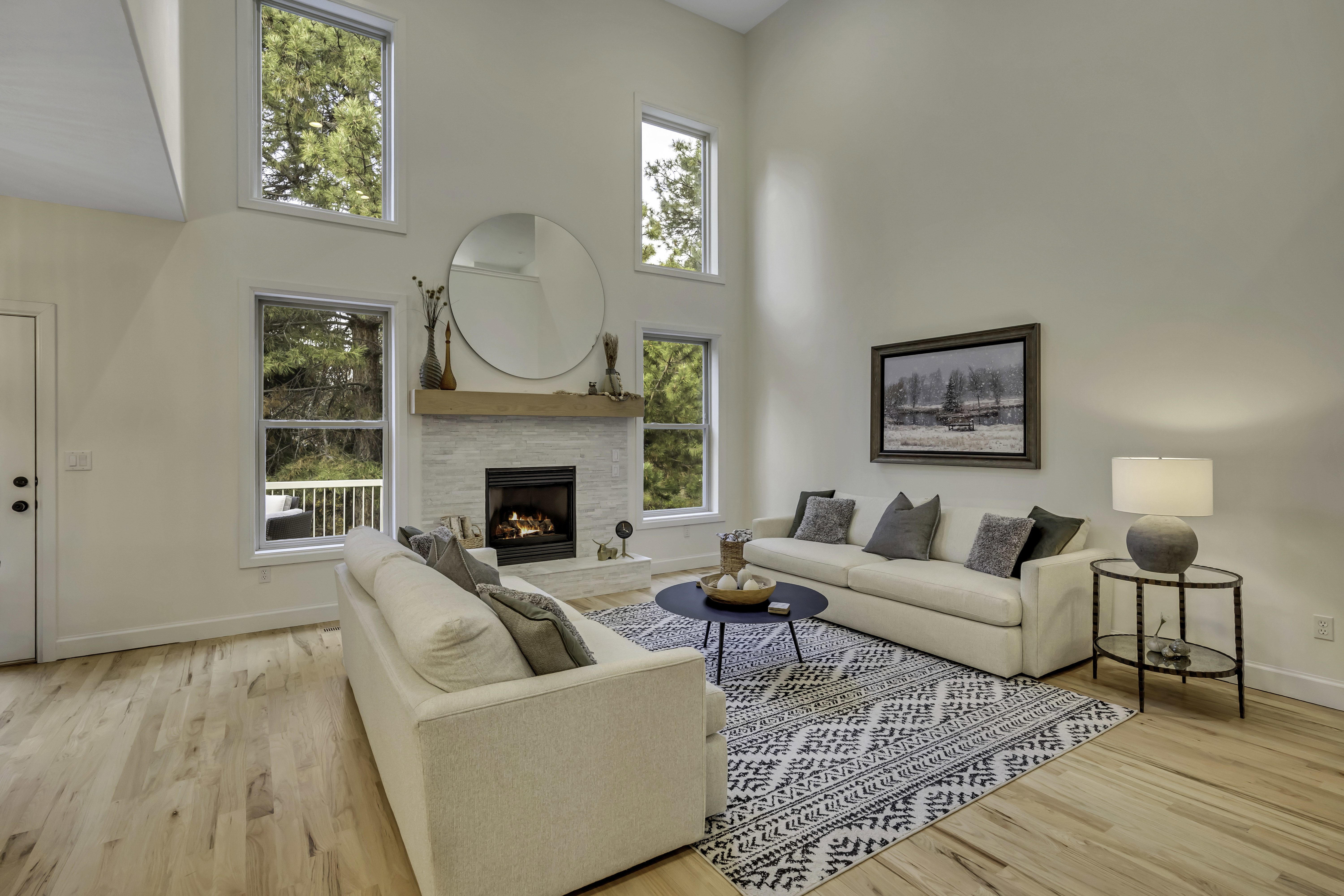 Vaulted ceiling living area featuring light wood-finish flooring, a contemporary fireplace with a stone surround and wood mantel, and multiple large windows