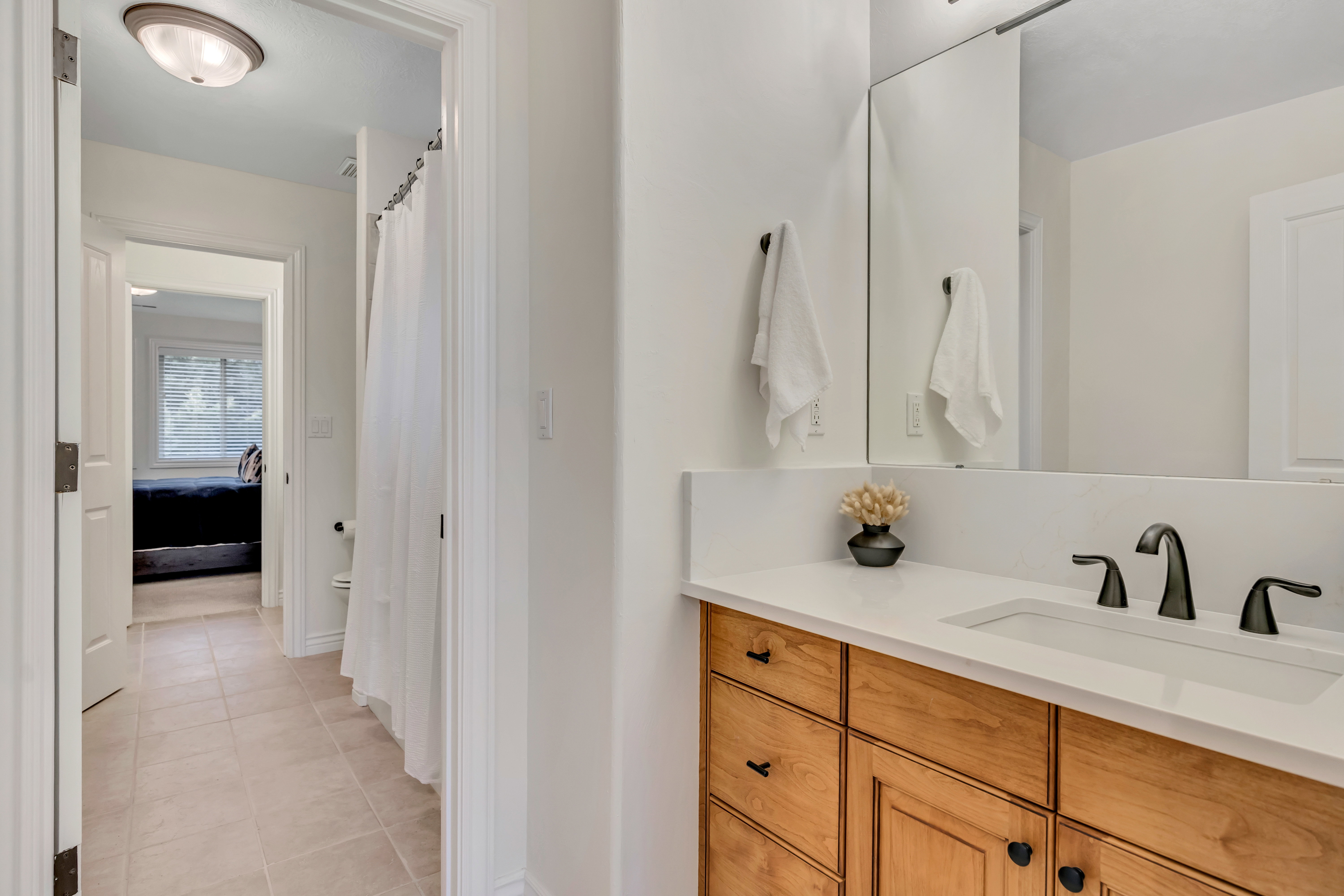 Bathroom vanity with light wood-finish cabinetry, a white countertop, and a built-in sink with a matte black faucet