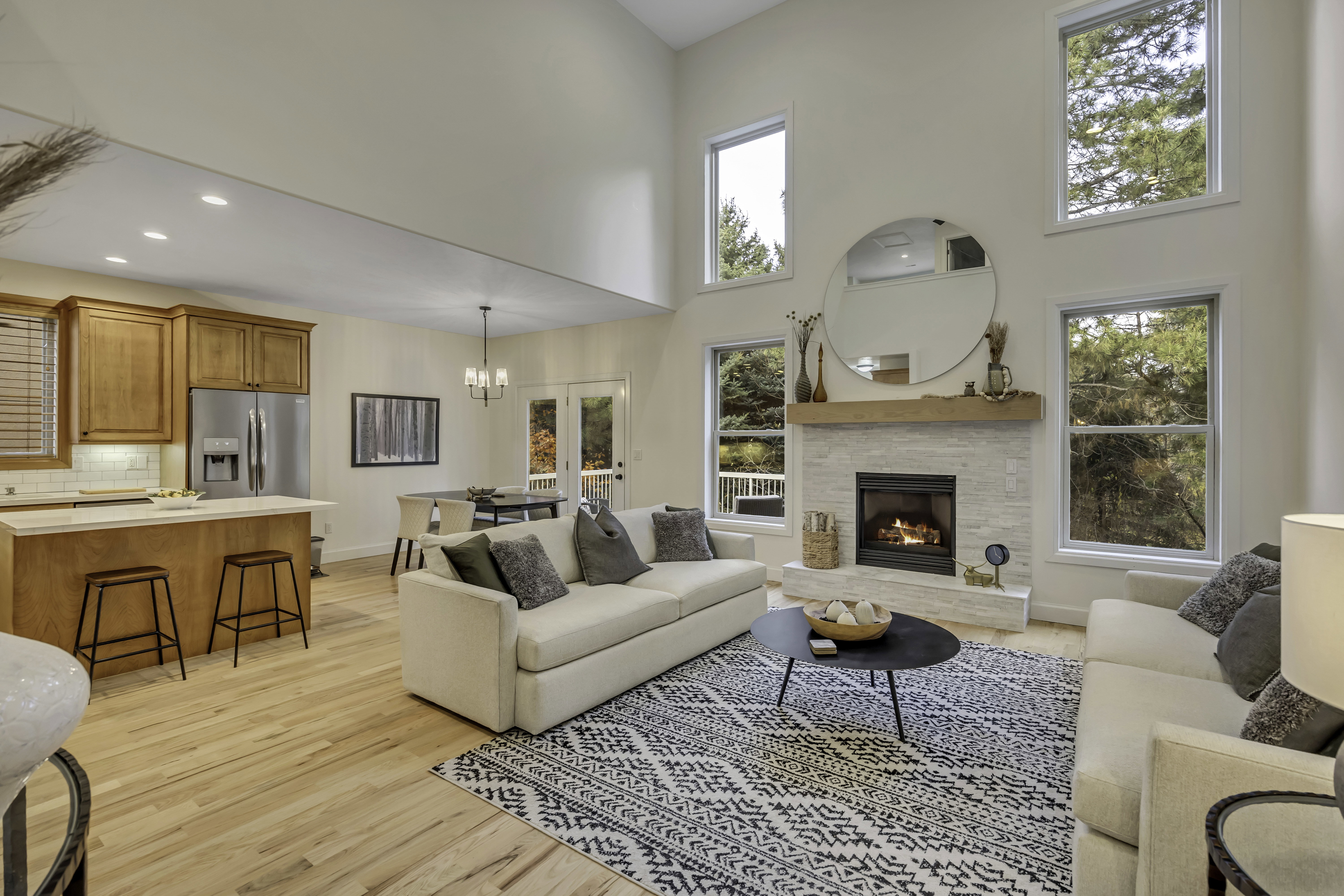 Vaulted living space featuring a stone fireplace with a wood mantle, multiple tall windows, and light wood-finish flooring