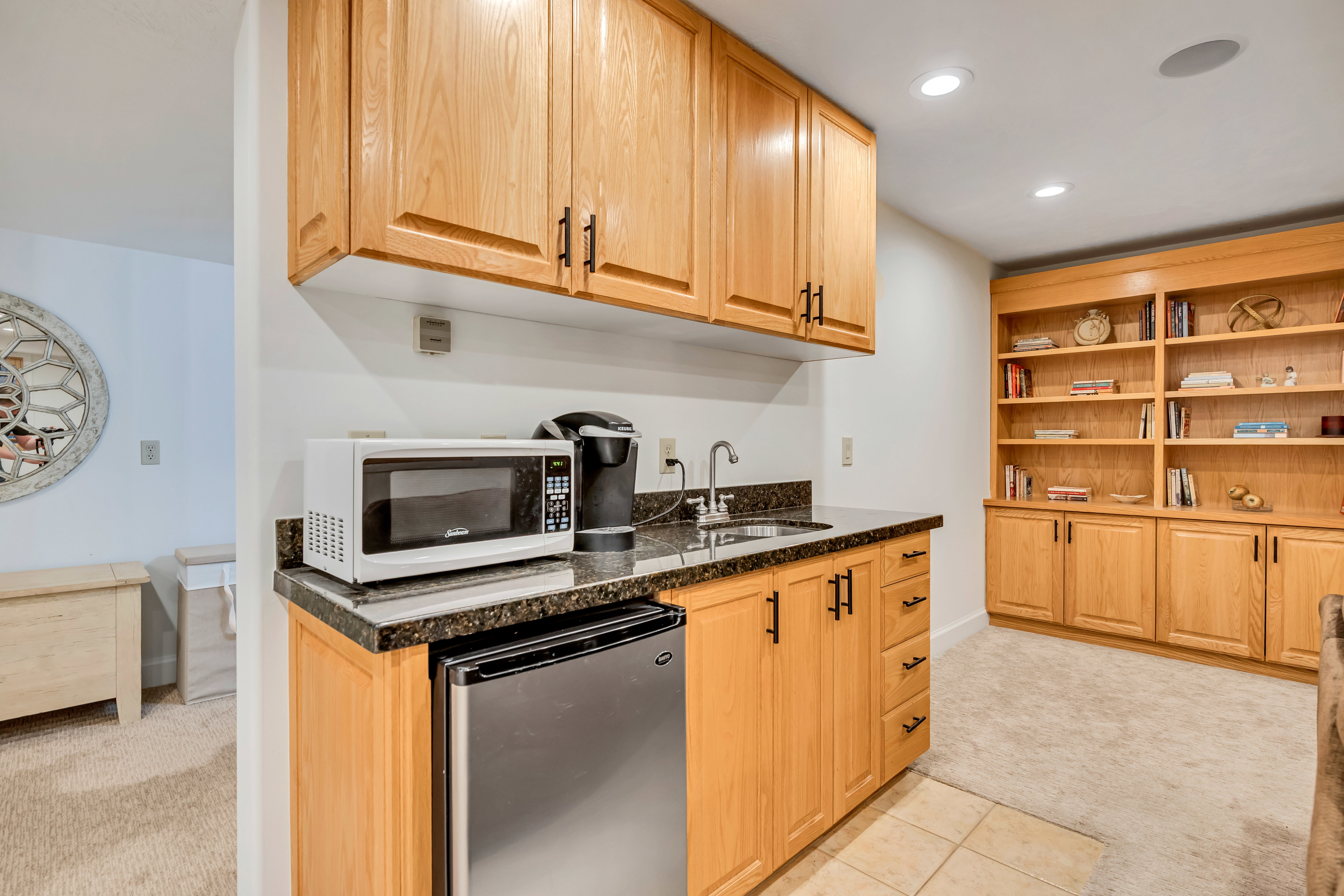 Compact kitchenette featuring wood cabinetry, dark speckled countertops, and a stainless steel under-counter refrigerator