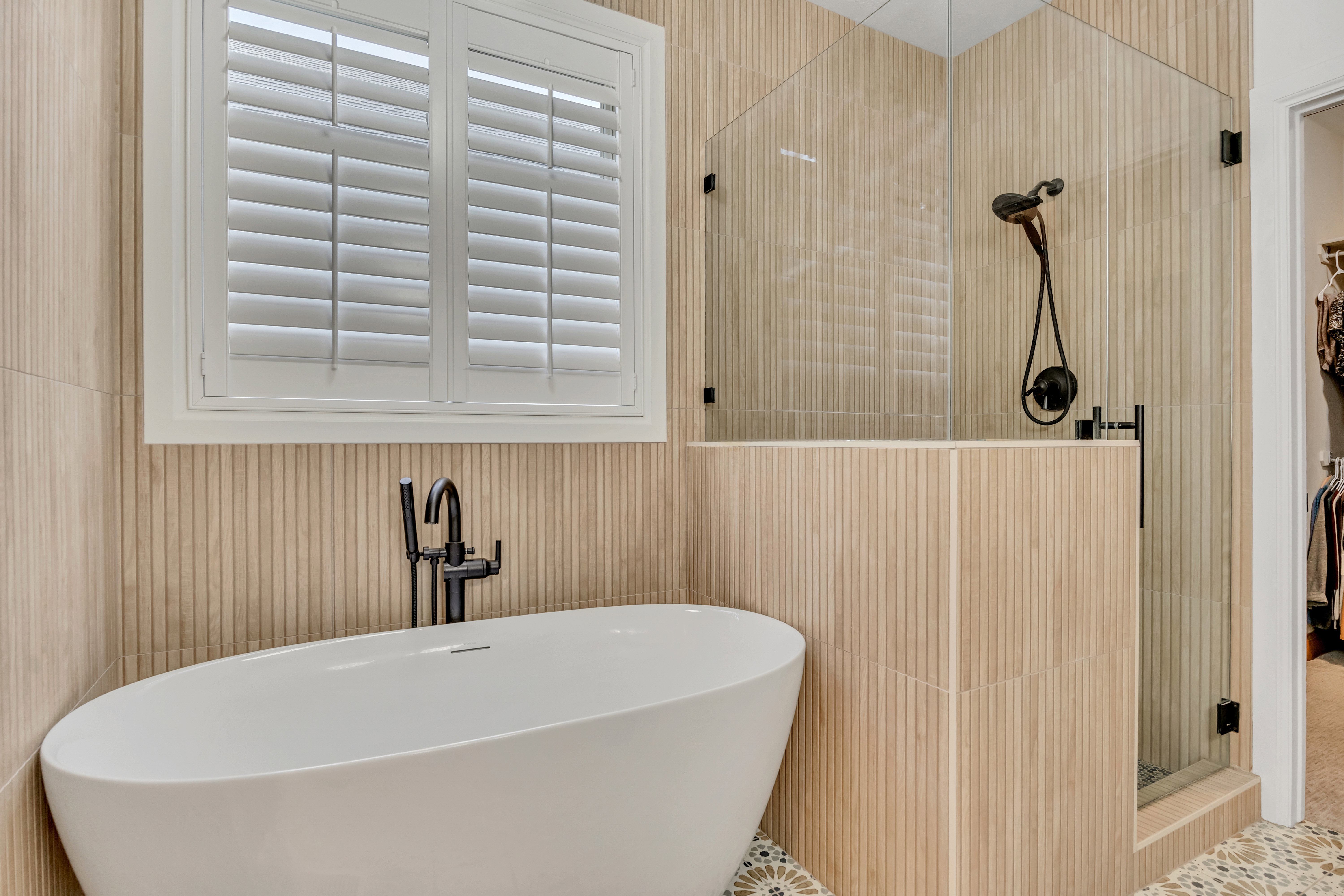 Freestanding soaking tub with a floor-mounted matte black faucet, surrounded by fluted wall tile