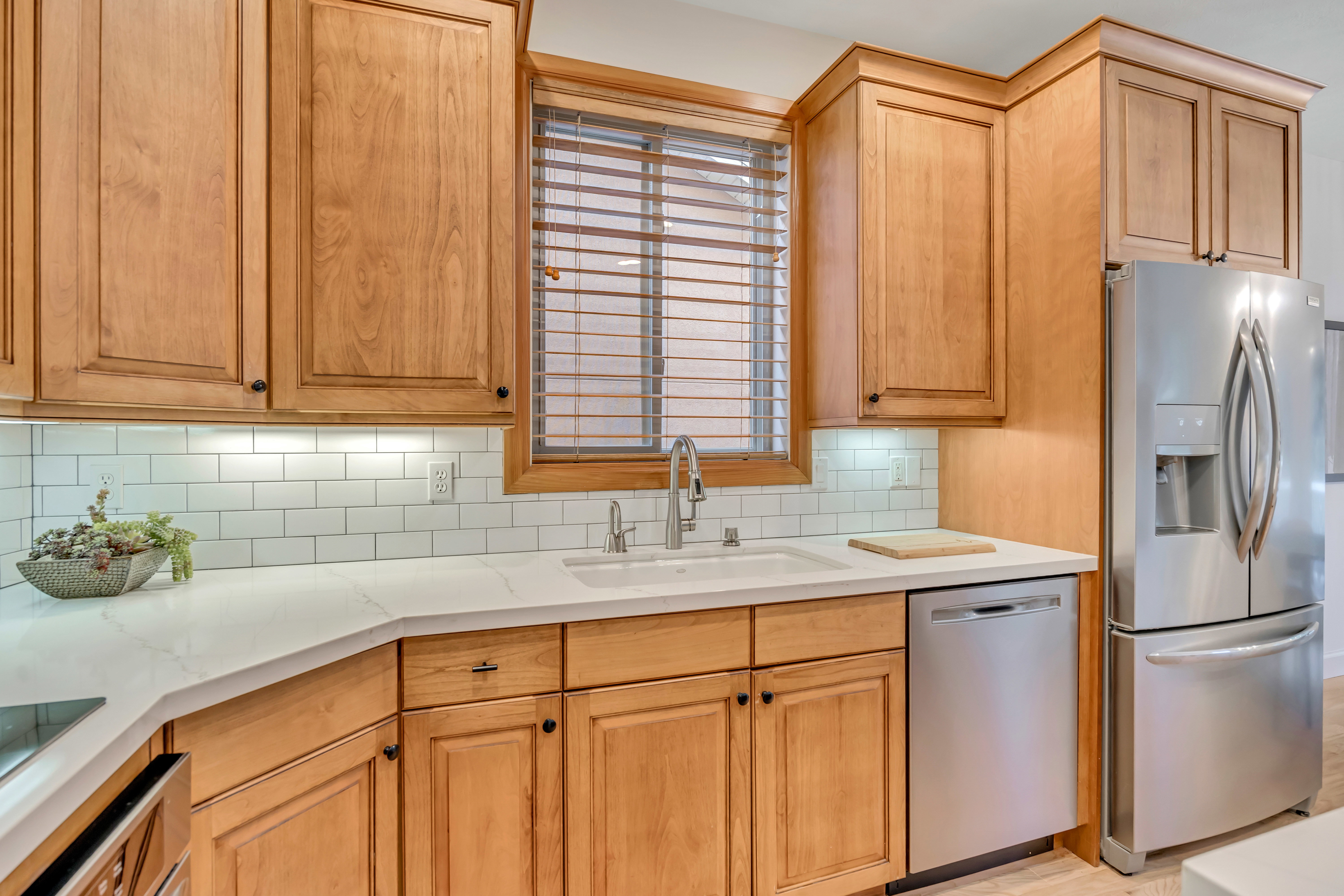 Kitchen featuring wood-finish cabinetry, white subway tile backsplash, white countertops, and stainless steel appliances including a refrigerator and dishwasher