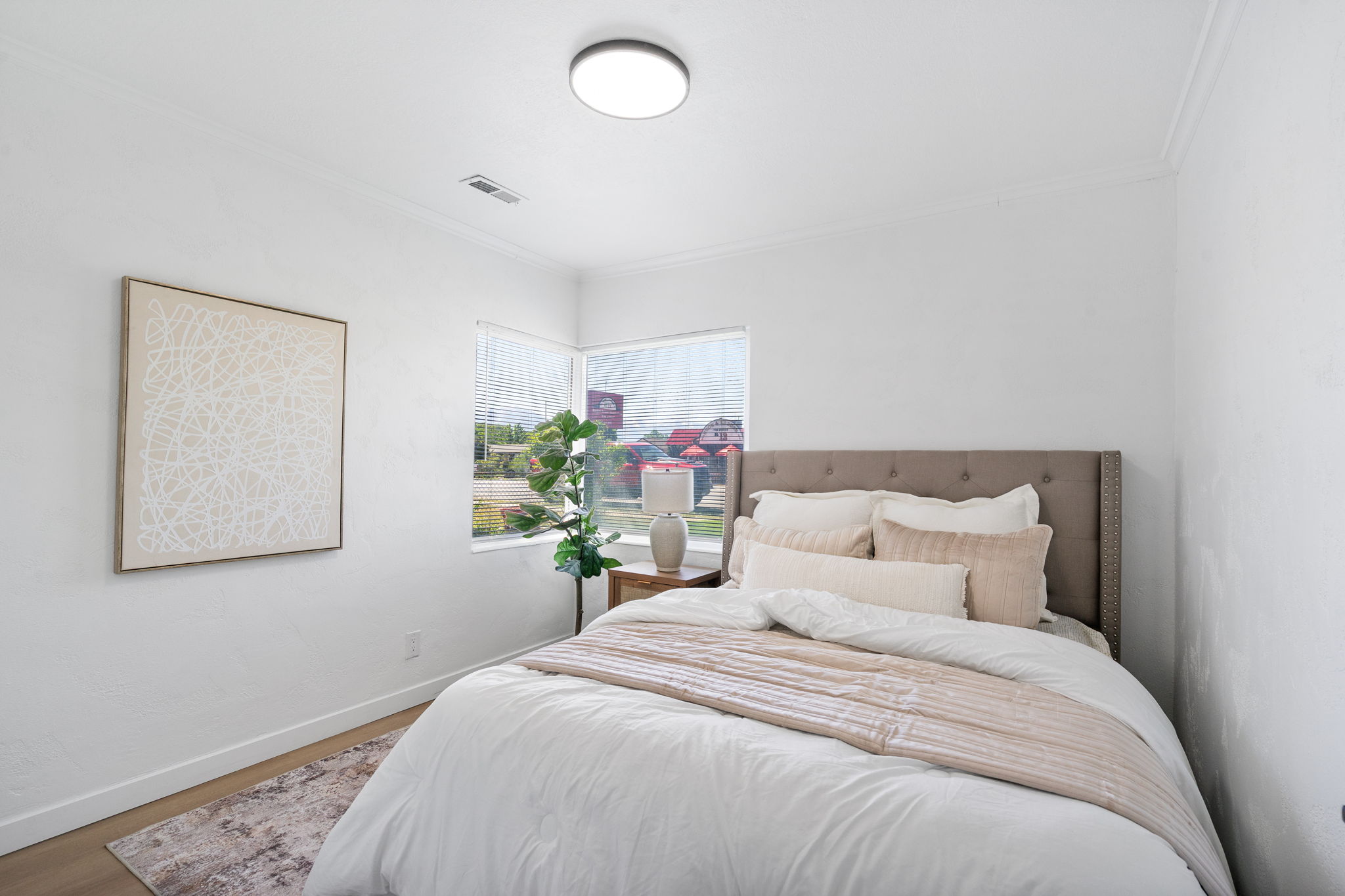 Bright bedroom featuring corner windows, wood-finish flooring, a contemporary flush-mount ceiling light, crown molding, and white baseboards