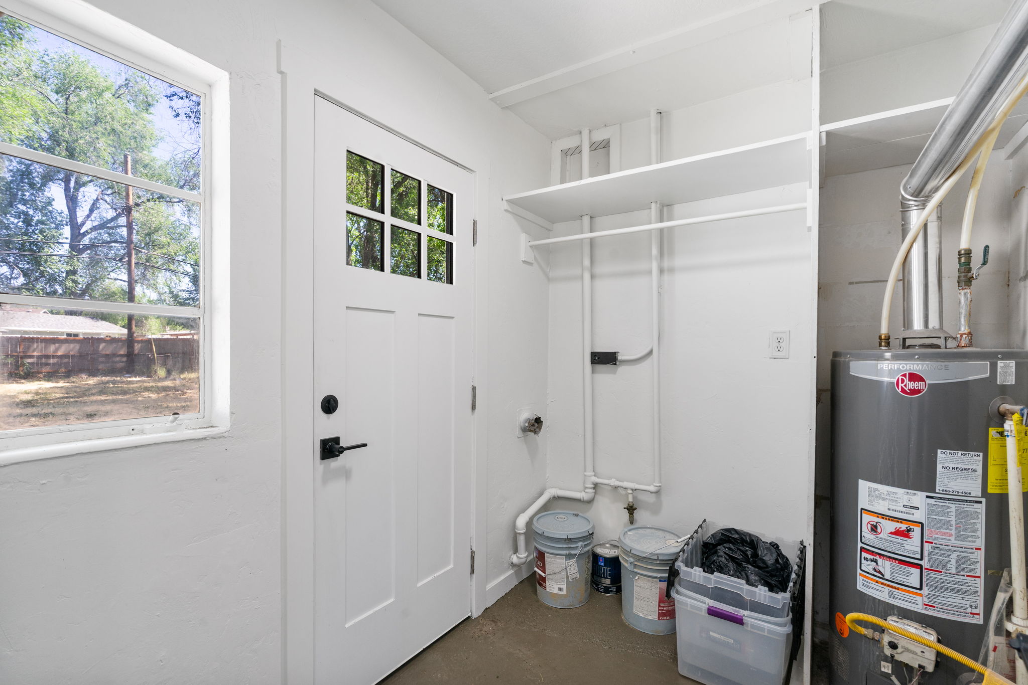 Utility area featuring a white door with divided lites, a single-pane window, built-in shelving, a clothes hanging rod, and a water heater