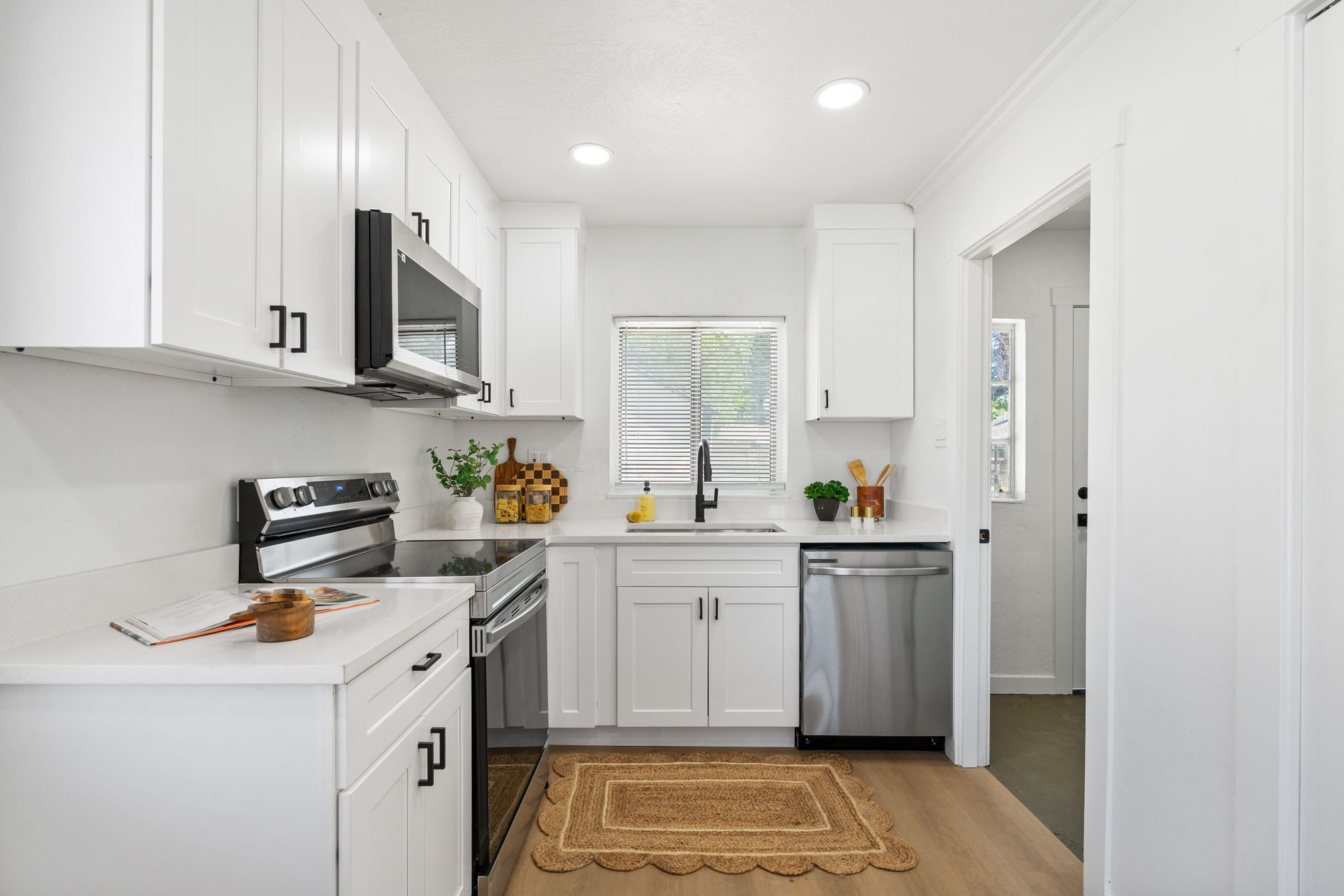 Modern kitchen featuring white shaker cabinetry, stainless steel appliances, light-colored countertops, and wood-finish flooring