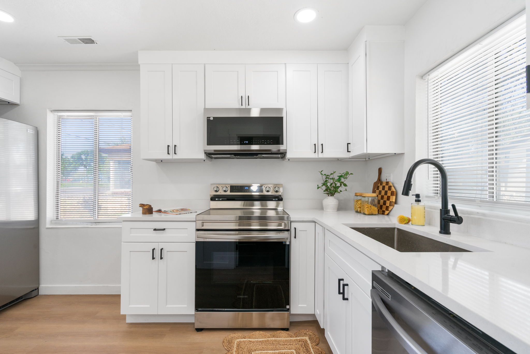 Contemporary kitchen featuring white shaker cabinetry, stainless steel appliances, a matte black faucet, and wood-finish flooring