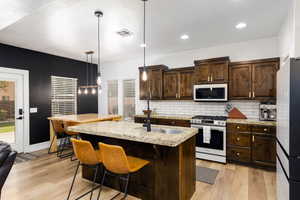 Kitchen featuring wood-finish flooring, dark wood cabinetry with gold-tone hardware, granite countertops, and a subway tile backsplash