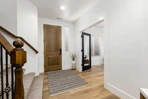 Entryway featuring a wood-panel door, light wood-finish flooring, and a carpeted staircase with an ornamental iron railing
