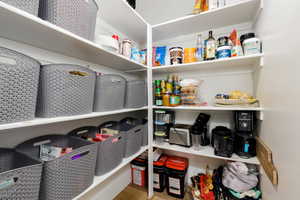 Walk-in pantry with extensive shelving, white painted walls, and wood-finish flooring