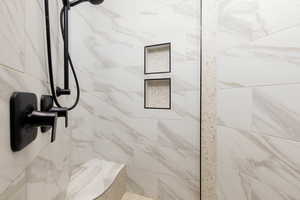 Shower featuring matte black fixtures, marble-look wall tile, built-in shower bench, recessed shower niches, and pebble-tile accent strip