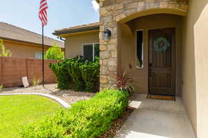 Inviting entryway featuring a wood-panel door, stone accent column, concrete walkway, and manicured landscaping with a block wall
