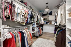 Walk-in closet featuring extensive built-in shelving, multiple hanging rods, wood-finish flooring, and a contemporary ceiling light fixture