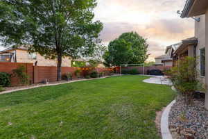 Spacious backyard featuring a large grass area, mature trees, a concrete patio, and a rock-lined border