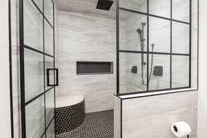 Spacious shower enclosure with black-framed glass panels, featuring light-toned tile walls, dark hexagonal tile flooring, a built-in shower bench, and a recessed niche with matching hexagonal tile