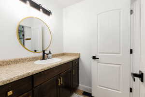Bathroom vanity featuring a speckled countertop, dark wood-finish cabinetry with gold-tone hardware, and an oval undermount sink with a matte black faucet