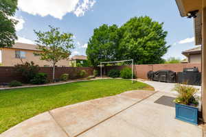Expansive backyard featuring a large concrete patio, lush green lawn, mature trees, and a privacy wall