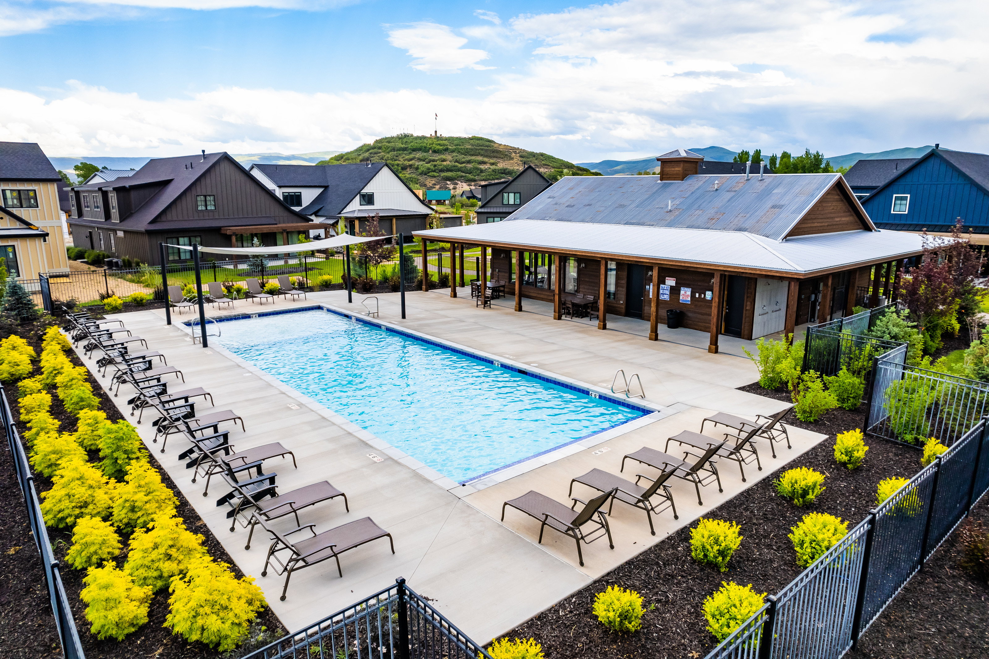 Resort-style swimming pool with surrounding patio space, a dedicated clubhouse building, and mature landscaping