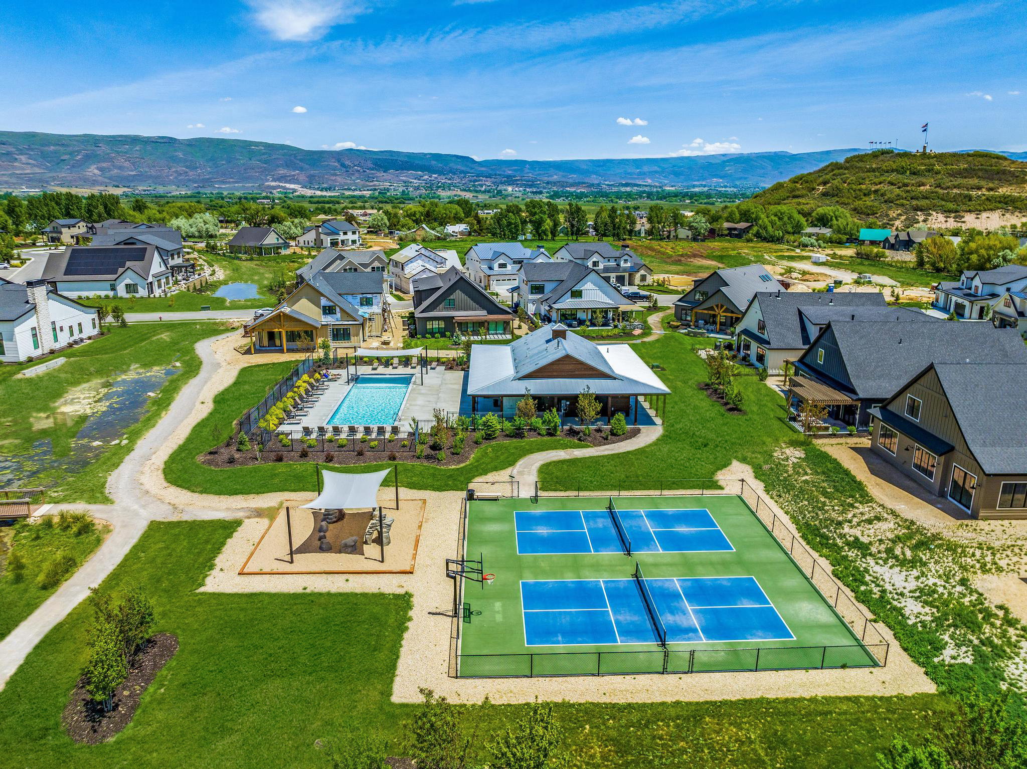 Community recreational area featuring a swimming pool, covered patio, two pickleball courts, and a shaded play area