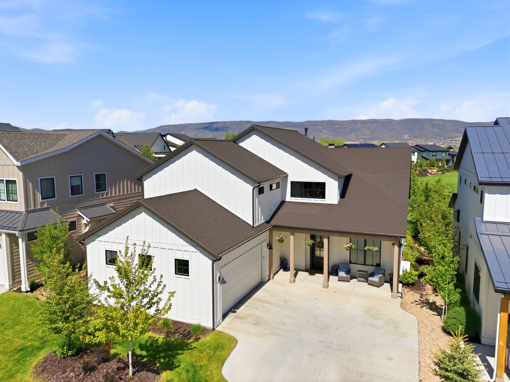 Contemporary residence featuring white board and batten siding, dark shingle roofing, and a prominent two-car garage