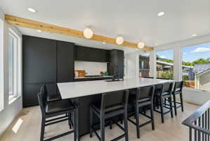 Contemporary kitchen featuring an expansive island with a white countertop and built-in sink, integrated black cabinetry, light wood-finish flooring, and multiple recessed and pendant light fixtures