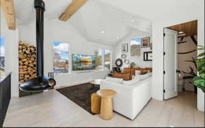 Vaulted ceiling living space featuring a suspended modern fireplace, exposed wood beams, light wood-finish flooring, and multiple windows