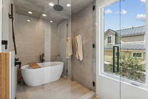 Contemporary bathroom featuring a freestanding soaking tub, a rain showerhead, a glass-enclosed shower, and recessed ceiling lighting