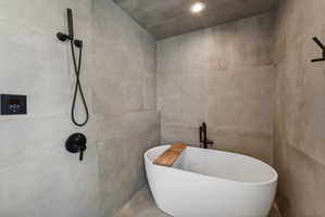 Freestanding soaking tub with matte black fixtures, surrounded by large format tile walls and flooring
