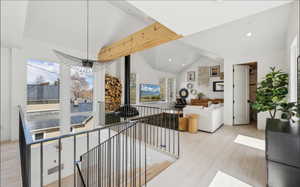 Vaulted ceilings featuring exposed wood beams, a modern pendant light fixture, and light wood-finish flooring